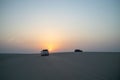 Rear view of white Jeep driving through white sandy desert during sunset