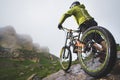 Rear view wide angle of a man on a mountain bike stands on a rocky terrain and looks at a rock. The concept of a