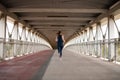 Rear view of woman athlete in suitable sports clothes running on modern urban footbridge