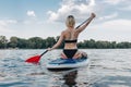 rear view of woman in black bikini sitting on paddle board