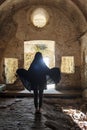 Rear view of woman in black cape in old abandoned chapel