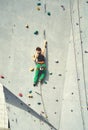 Rear view woman climber in bright green pants climbing on vertical artificial rock wall.