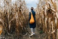 Rear view of a woman in a coat with a bright orange bag walking between rows of corn in a field in autumn