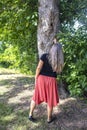 Rear view of woman in dress with long gray hair pointing up at a hole in a tree trunk