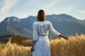 Rear view woman enjoying nature view of mountains, standing in golden field at sunset Royalty Free Stock Photo