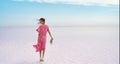 Rear view woman in flowing pink dress at inspiring paradise landscape of salt flats on pink lake