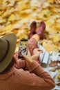 Rear view of woman in hat taking photo on camera phone while relaxing in autumn park Royalty Free Stock Photo