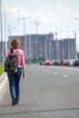 Rear view at woman hitchhiker walking on asphalt road in urban street, copyspace