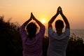 Rear view of woman and man folding palms together and lifting arms up watching at sunset, practicing yoga together. Royalty Free Stock Photo