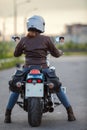 Rear view at woman motorcyclist sitting on the classic chopper motorbike on urban asphalt road