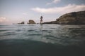 Rear view of woman paddling SUP board through passage between rocks Royalty Free Stock Photo