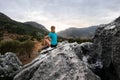 rear view on woman resting on stone and enjoying beautiful mountains landscape.