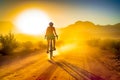 Rear view of a woman riding a bike. Bicyclist on the dirt road at sunset on summer day. Silhouettes of mountains at backdrop. Royalty Free Stock Photo