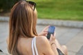 Rear view of woman sitting on a bench, holding a smart phone while surfing the internet, young woman texting on her cell