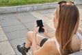 Rear view of woman sitting on a bench, holding a smart phone while surfing the internet, young woman texting on her cell