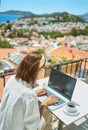 Rear view woman using laptop computer working typing online over Mediterranean view from outside balcony Royalty Free Stock Photo