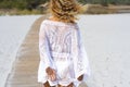 Rear view of woman walking on sand in beach. Back of woman tourist in white dress walking on footpath amidst sand at beach. Female