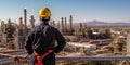 Rear view of a worker at the top of an oil refinery, looking out over the complex network of pipes and tanks , concept