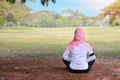 Rear view young asian muslim woman sitting on grass, enjoying meditation. Peaceful girl in sportswear with pink hijab practice