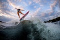 Rear view of young attractive woman who stands on surf style wakeboard and jumps on wave. Royalty Free Stock Photo