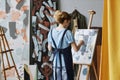 Rear view of young blond female painter creating new artwork on canvas