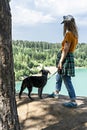 Rear view of young blond woman traveler in a cap and ginger t-shirt standing on the cliff of blue turquoise lake or river and