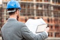 Rear view of a young engineer or architect looking over building blueprints and using a tablet Royalty Free Stock Photo