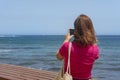 Rear view of a young Caucasian woman taking pictures of the marine vistas in front of her Royalty Free Stock Photo