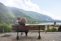 Rear view of a young couple sitting and hugging on a Bench in front of the mountain lake. The man is embracing her girlfriend Royalty Free Stock Photo