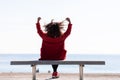 Rear view of a young curly woman wearing red denim jacket sitting on a bench while looking away to horizon over sea Royalty Free Stock Photo