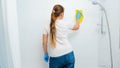 Rear view of young funny woman dancing while washing walls in bathroom and doing housework or home cleanup