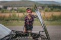 Rear view of young girl in gray short denim shorts is repairing the car. In shorts near a black car with open hood. Problems with