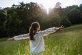 Rear view of young girl standing on meadow with open arms, enjoying warm spring day. Royalty Free Stock Photo