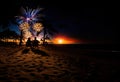 Rear view of young happy couple in love sitting on beach and watching fireworks at sunset Royalty Free Stock Photo