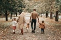 Rear view of young happy family walking in autumn park. Mother father son daughter and dog labrador walking through the forest. Royalty Free Stock Photo