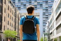 Rear view of a young man with backpack just arrived in a big city and looking to modern buildings with perspectives and