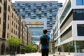 Rear view of a young man with backpack just arrived in big city and looking to modern buildings with perspectives and