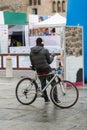 Rear View of Young Man with EarPhones Sitting on Bicycle and Using Smartphone on City Street: People, Style, Technology, Leisure