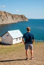 Rear view a young man in front of a white lonely house on the edge of a cliff with a picturesque mountain landscape and a view of Royalty Free Stock Photo