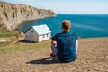 Rear view a young man in front of a white lonely house on the edge of a cliff with a picturesque mountain landscape and a view of Royalty Free Stock Photo