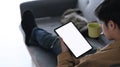 A young man using tablet checking social media and drinking coffee while sitting on sofa at home. Royalty Free Stock Photo