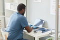 Rear view of young modern clinician in blue uniform typing on laptop keyboard