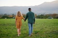 Rear view of young multiracial couple holding hands while walking in field Royalty Free Stock Photo