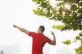 Rear view of young muscular man stretching by a tree, arms raised and fingers pointing towards the sky in Beijing, China with lens Royalty Free Stock Photo