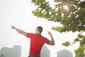 Rear view of young muscular man stretching by a tree, arms raised and fingers pointing towards the sky in Beijing, China with lens