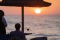 Rear view of a young romantic couple drinking cocktails and wine on a tropical beach at sunset on vacation or honeymoon Royalty Free Stock Photo