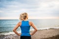 Rear view of young sporty woman runner in blue sportswear standing on the beach. Royalty Free Stock Photo