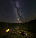 Couple sitting around the campfire admiring the mountains under the starry sky during the night camping Royalty Free Stock Photo