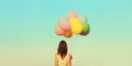 Rear view of young woman with bunch of colorful balloons in field outdoors on blue sky background Royalty Free Stock Photo