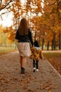 Rear view on a young woman in a fashion dress and a child in stylish clothes in the park. Mom and baby walks in the autumn park on